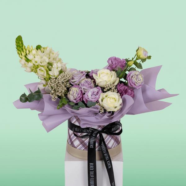 Purple and white Roses, Eustoma, Ornithogalum, Rice Flowers and Eucalyptus arranged in a small round box.
