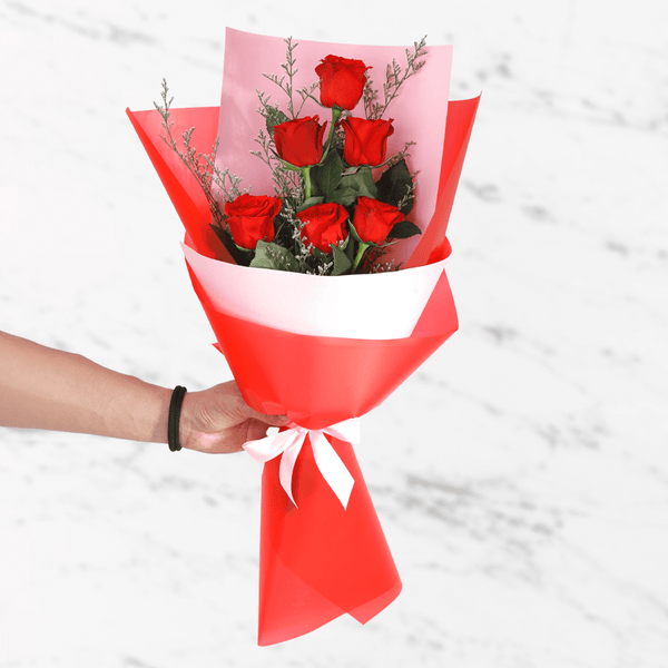 A bouquet of 6 fresh red roses in white and red wrap tied with a red ribbon.