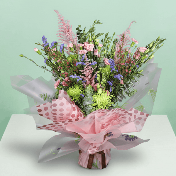 A pink bouquet of disbuds, spray roses, Eustoma, statice and astilbe with greenery in pink Korean-style flower sheets