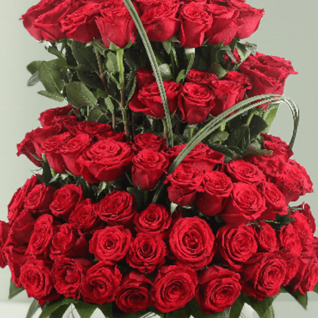 Multi-tier arrangement of 101 red roses with greenery in a transparent glass fishbowl vase