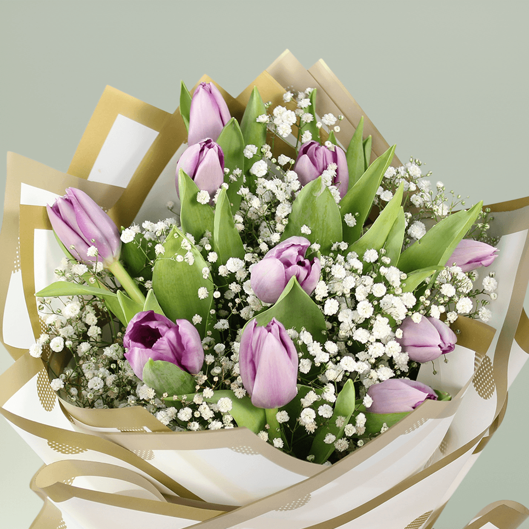 Purple tulip bouquet with baby’s breath, green foliage and elegant gold-accented wrapping.