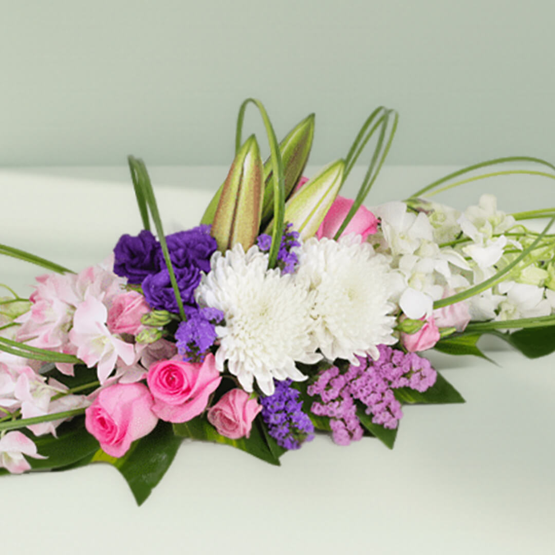 Purple orchids, pink roses and white chrysanthemums arranged with curved greenery on a long green tray