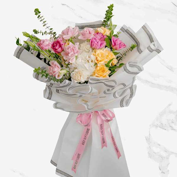 Pastel hand bouquet with pink and peach roses, white lilies, hydrangeas and eucalyptus in elegant grey wrapping.