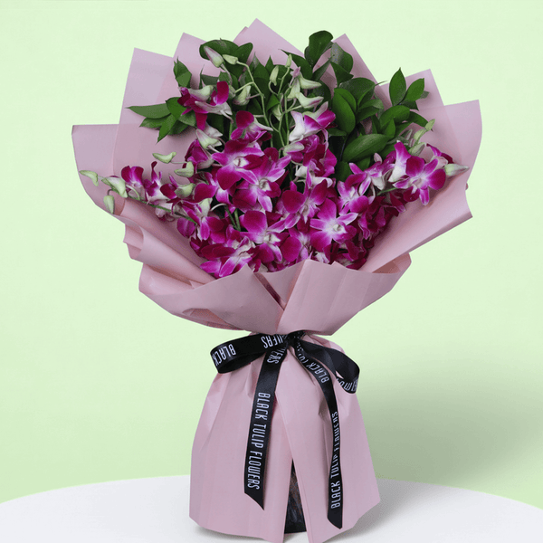 10 purple dendrobium orchids bouquet with greenery in pink wrapping and black ribbon