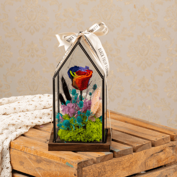 Preserved rainbow roses with dried flowers displayed in a clear glass dome.