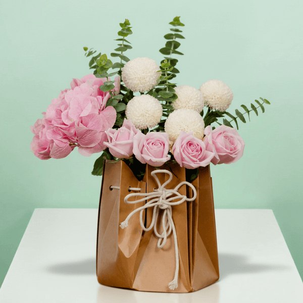 Mixed hydrangeas, roses, ping pong flowers and eucalyptus arranged in a rustic paper bag.