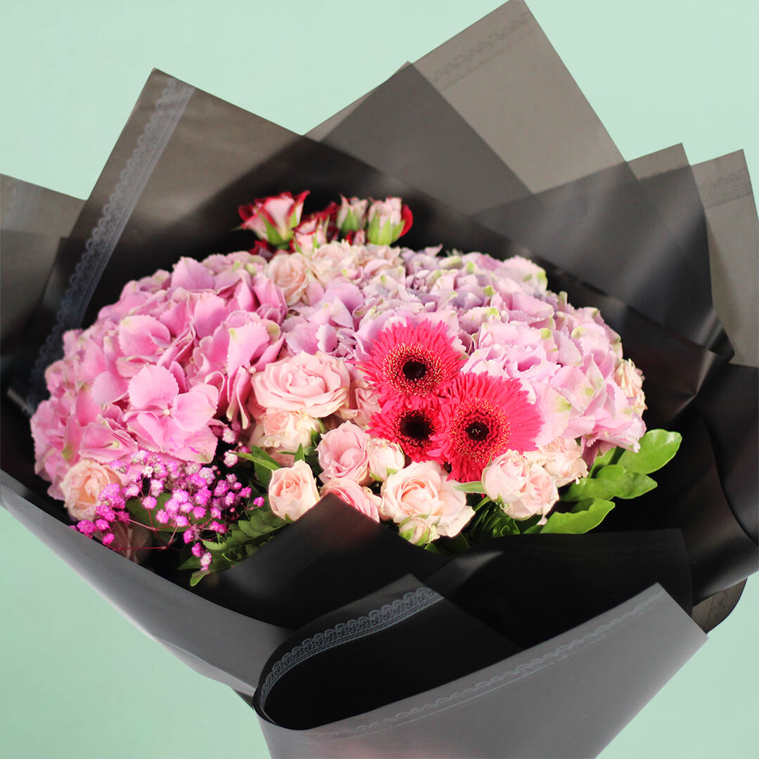 Pink Hydrangeas, Spray Roses, Gerberas and Gypsophila wrapped in black non-woven paper.