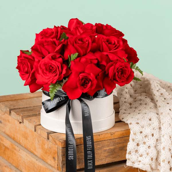 Fresh red roses arranged in a white round flower box with black ribbon