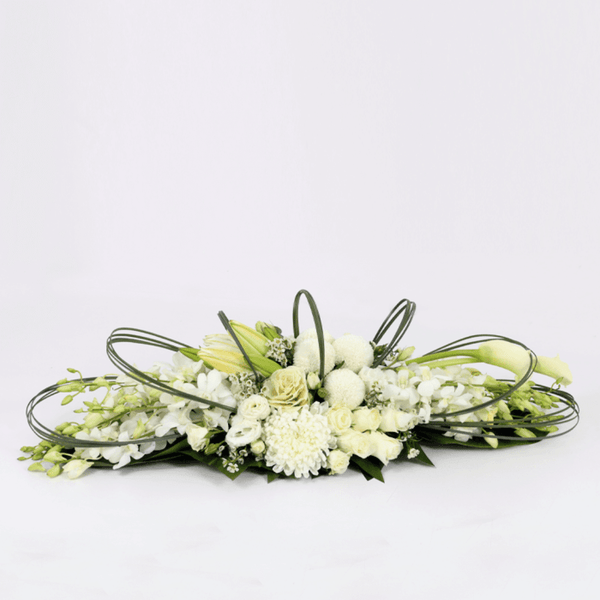 White orchids, lilies, roses, disbuds and chrysanthemums arranged with curved greenery on a long green tray