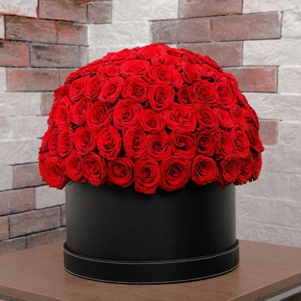 Large dome arrangement of red roses displayed in a black round hat box