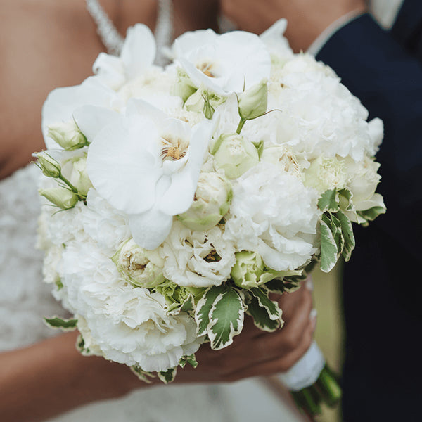 A rounded style bridal bouquet of white Phalaenopsis orchids, roses, seasonal flowers and variegated greenery.