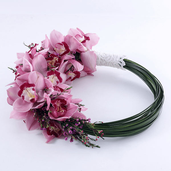 A loop-style bridal bouquet featuring pink Cymbidium orchids and delicate accent flowers in finished with a white lace handle.