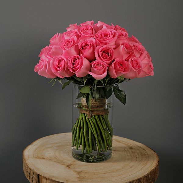 An elegant display of 30 pink roses and fresh greenery presented in a sleek transparent cylinder vase.
