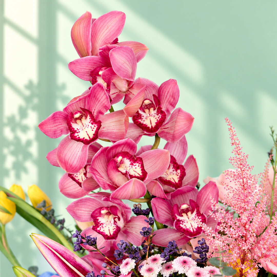 Pink round flower box featuring 50–60 stems of assorted hydrangeas, peonies, sunflowers, tulips, roses, lilies, cymbidium orchids and eucalyptus greenery.