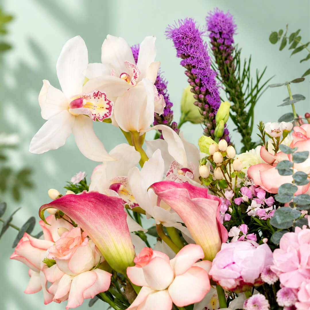 Assorted flowers including roses, hydrangea, calla lily, cymbidium, and Queen Protea arranged in a rectangular basket