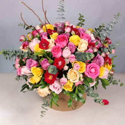 Assorted Roses and Spray Roses in a round flower box with Gemstone Rakhi and Ferrero Rocher chocolates.
