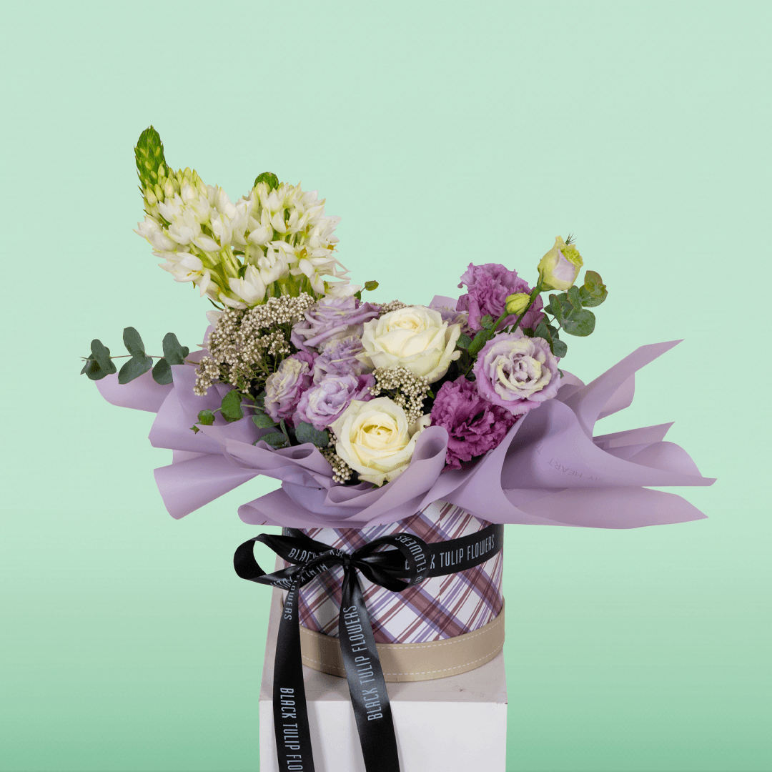 Purple and white Roses, Eustoma, Ornithogalum, Rice Flowers and Eucalyptus arranged in a small round box.