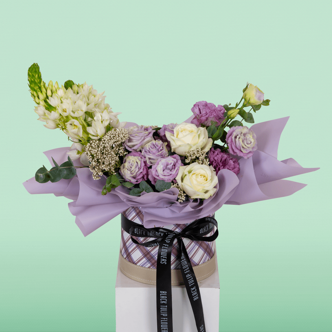Purple and white Roses, Eustoma, Ornithogalum, Rice Flowers and Eucalyptus arranged in a small round box.