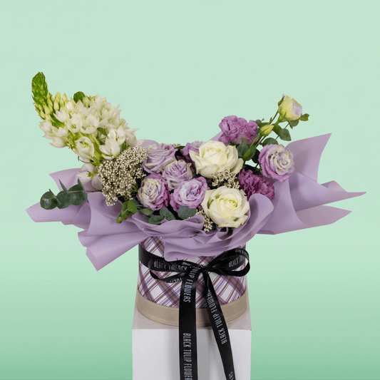 Purple and white Roses, Eustoma, Ornithogalum, Rice Flowers and Eucalyptus arranged in a small round box.