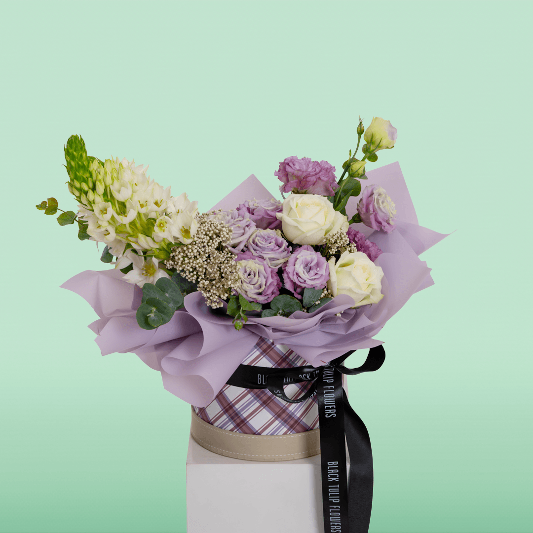 Purple and white Roses, Eustoma, Ornithogalum, Rice Flowers and Eucalyptus arranged in a small round box.