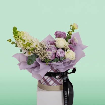 Purple and white Roses, Eustoma, Ornithogalum, Rice Flowers and Eucalyptus arranged in a small round box.