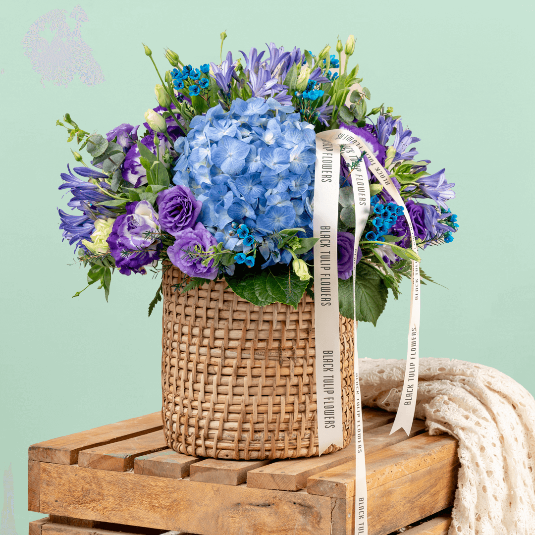 Blue and purple hydrangea, Eustoma, wax flower and agapanthus arrangement in a round basket