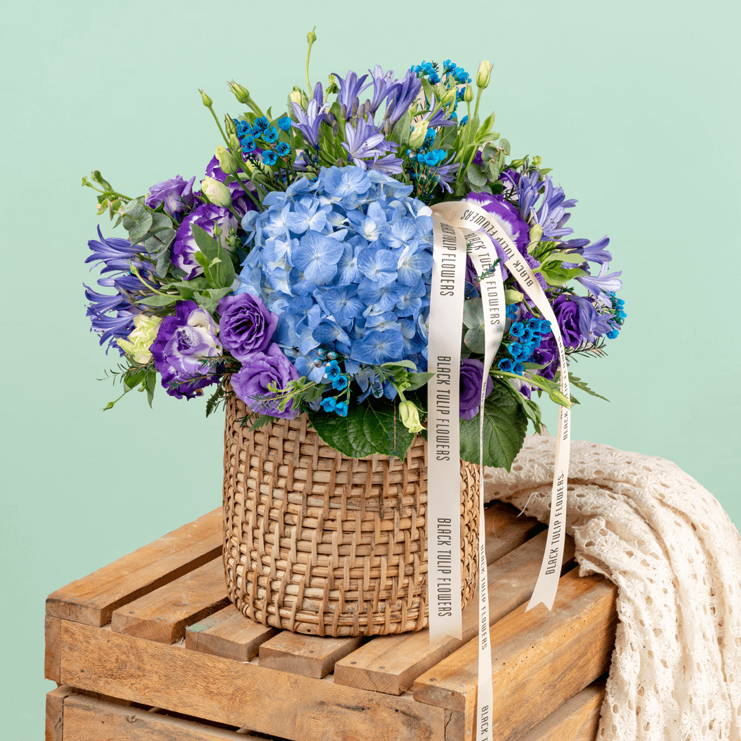 Blue and purple hydrangea, Eustoma, wax flower and agapanthus arrangement in a round basket