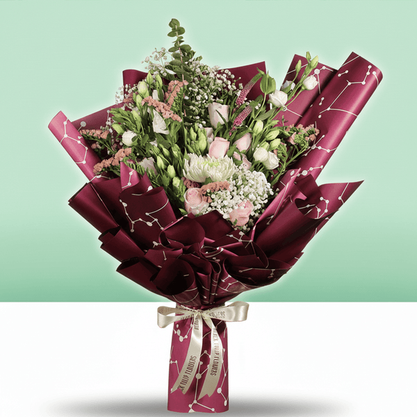 A bouquet of disbuds, Eustoma, roses and statice with fresh greenery wrapped in burgundy Korean-style flower sheets
