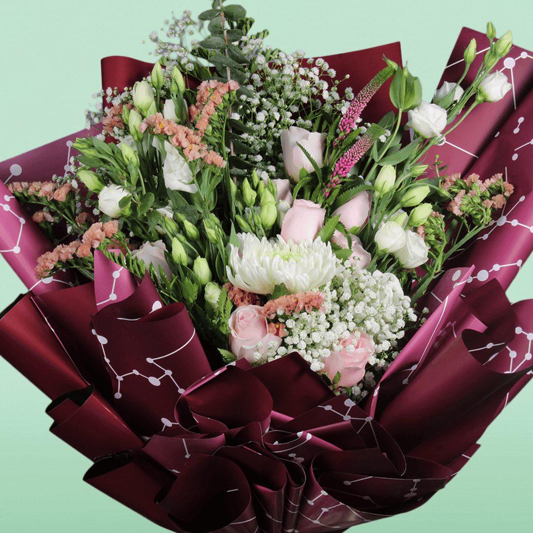 A bouquet of disbuds, Eustoma, roses and statice with fresh greenery wrapped in burgundy Korean-style flower sheets
