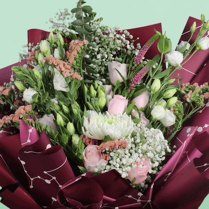 A bouquet of disbuds, Eustoma, roses and statice with fresh greenery wrapped in burgundy Korean-style flower sheets
