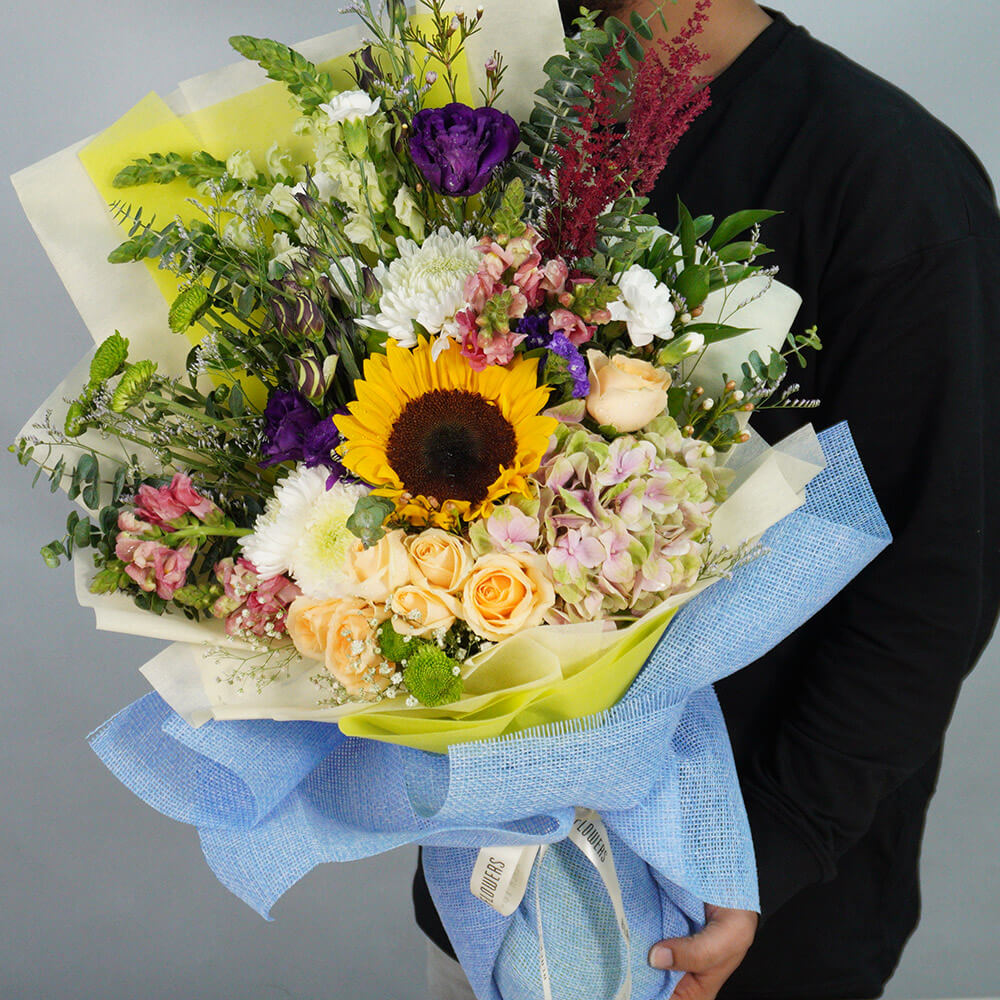 Mixed bouquet with Sunflower, Hydrangea, Roses, Snapdragon, Eustoma, Astilbe, Chrysanthemum, Wax Flower and greenery in blue wrap.