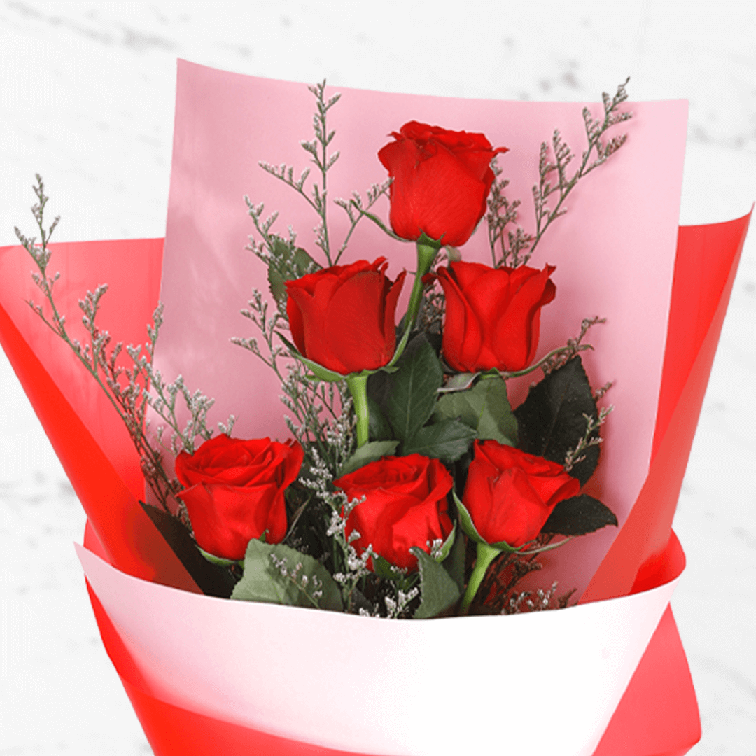 A bouquet of 6 fresh red roses in white and red wrap tied with a red ribbon.
