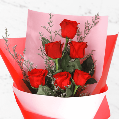 A bouquet of 6 fresh red roses in white and red wrap tied with a red ribbon.
