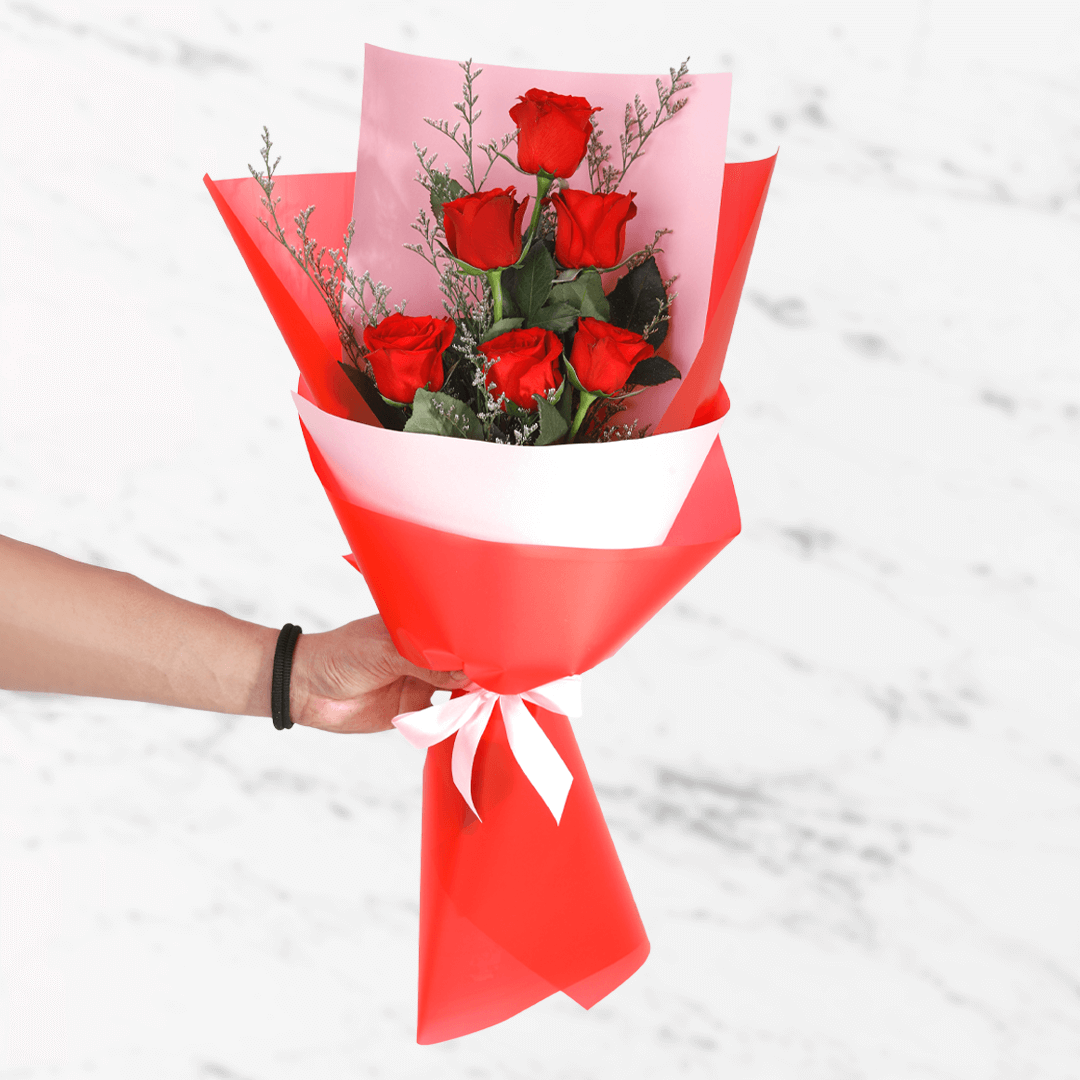 A bouquet of 6 fresh red roses in white and red wrap tied with a red ribbon.