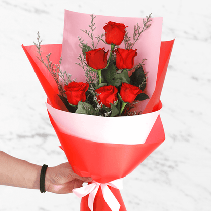 A bouquet of 6 fresh red roses in white and red wrap tied with a red ribbon.