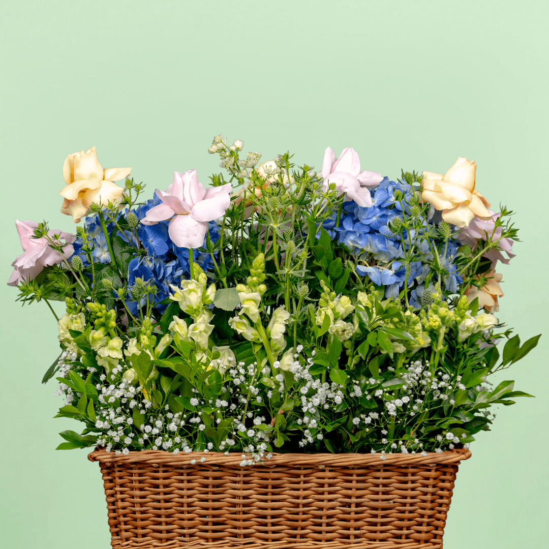Blue hydrangeas, pastel roses, Eustoma and greenery arranged in a woven flower basket