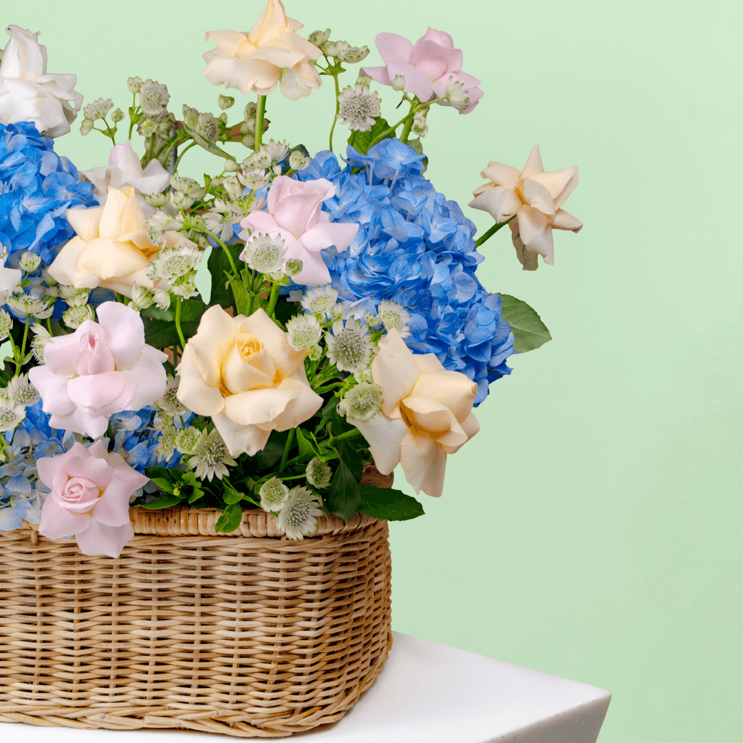 Blue hydrangeas, pastel roses, Eustoma and greenery arranged in a woven flower basket