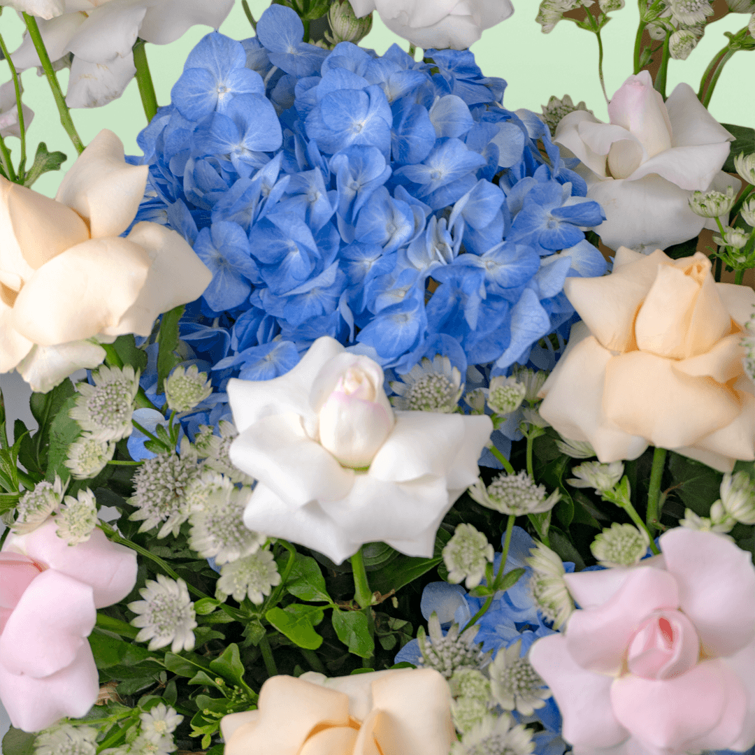 Blue hydrangeas, pastel roses, Eustoma and greenery arranged in a woven flower basket