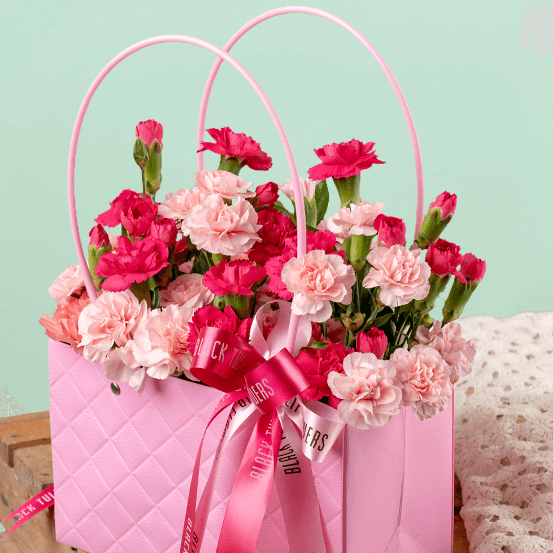 Pink and light pink carnations arranged in a quilted pink flower bag with ribbon details