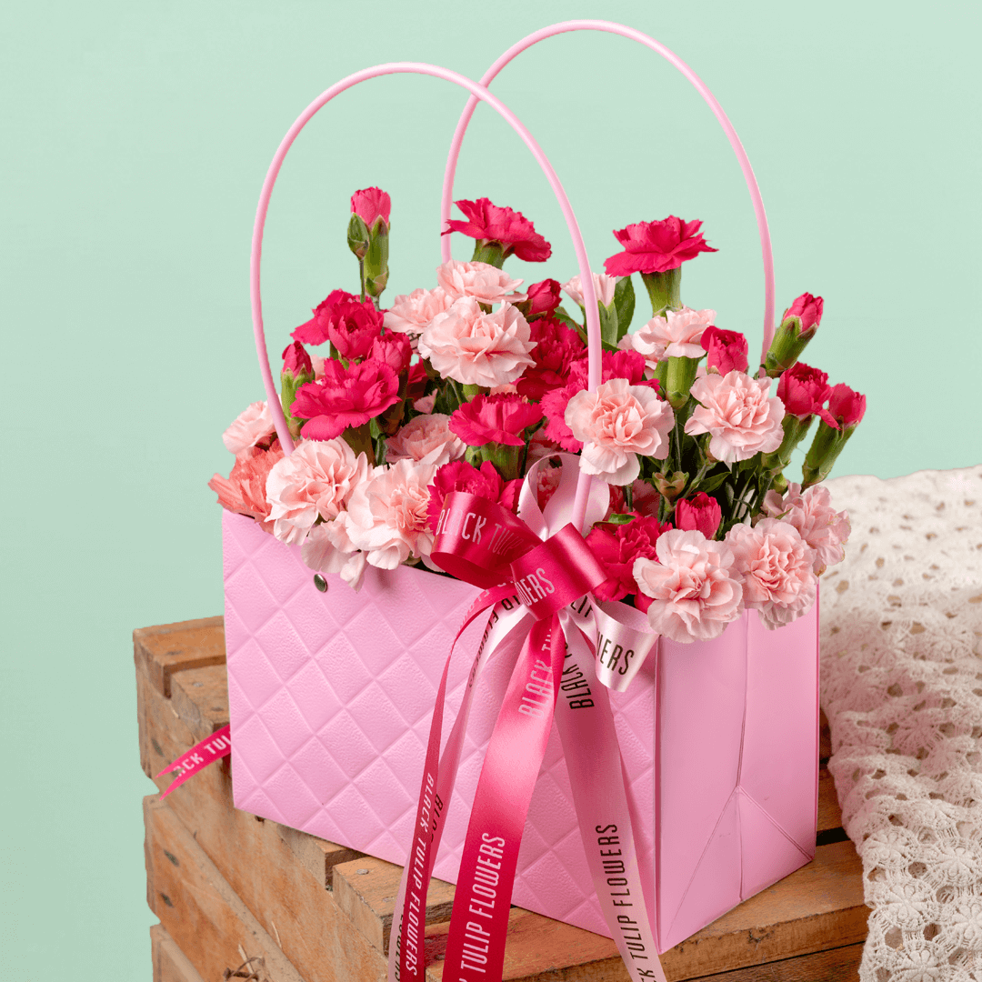 Pink and light pink carnations arranged in a quilted pink flower bag with ribbon details