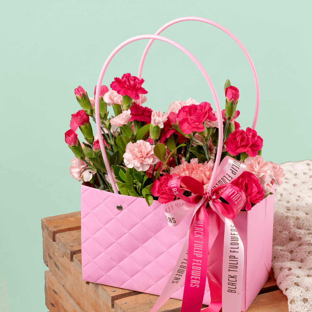 Pink and light pink carnations arranged in a quilted pink flower bag with ribbon details