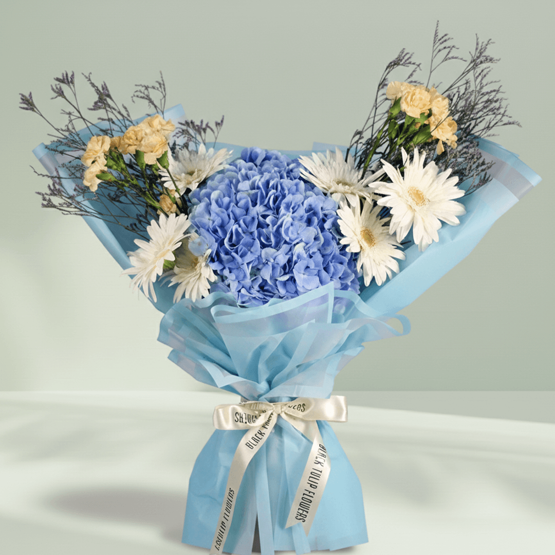 Blue Hydrangea with white Gerberas, cream Carnations and Limonium wrapped in blue non-woven paper.