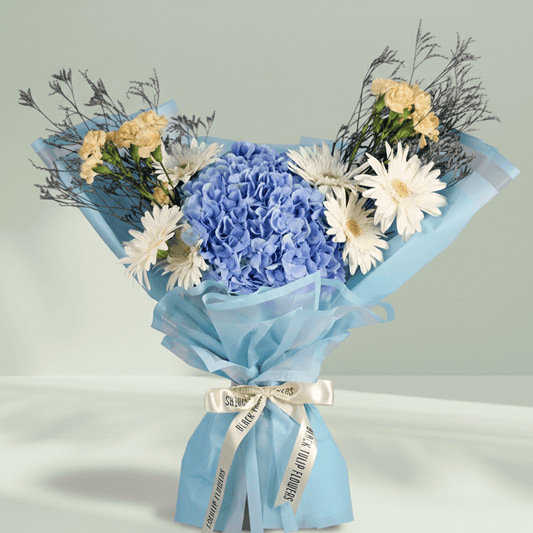 Blue Hydrangea with white Gerberas, cream Carnations and Limonium wrapped in blue non-woven paper.