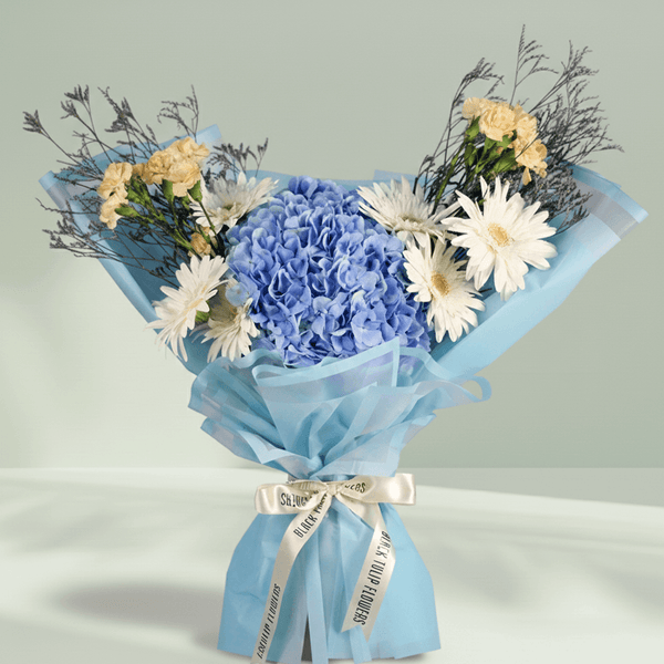 Blue Hydrangea with white Gerberas, cream Carnations and Limonium wrapped in blue non-woven paper.