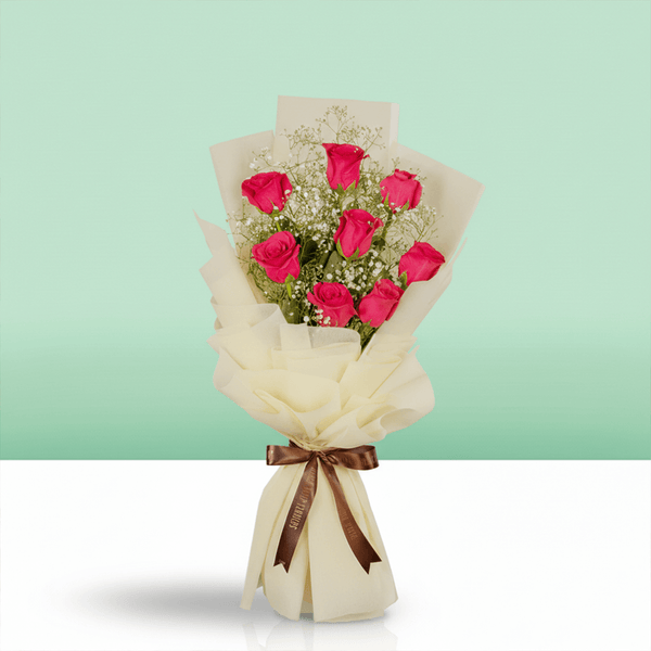 A bouquet of pink roses and gypsophila in layered cream wrapping, finished with a brown ribbon.