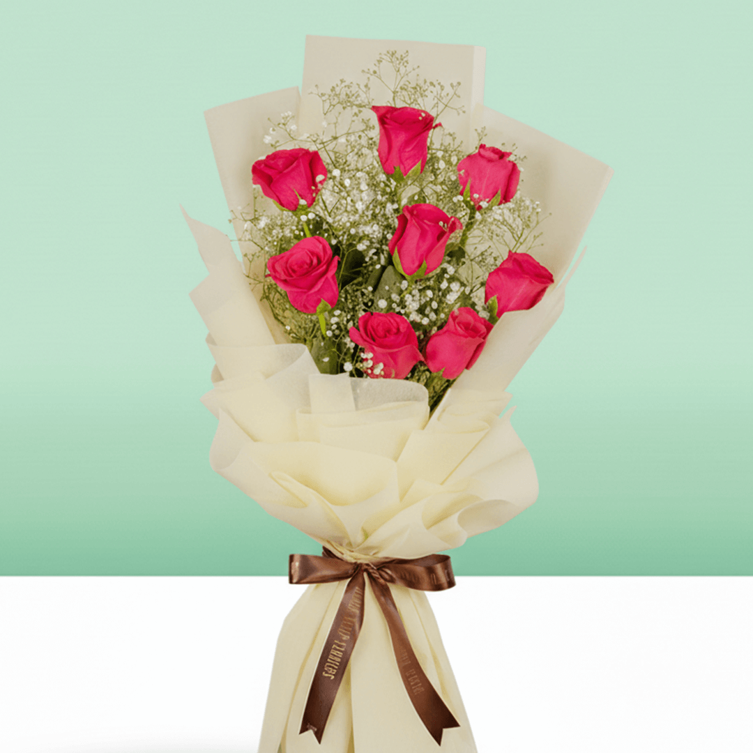 A bouquet of pink roses and gypsophila in layered cream wrapping, finished with a brown ribbon.