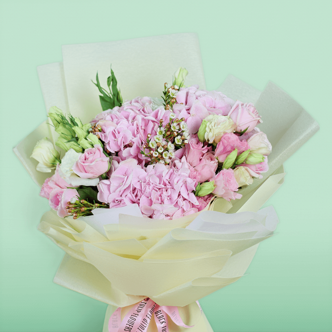 Bouquet of pink hydrangeas, roses, Eustoma and wax flowers arranged in layered ivory non-woven wrapping
