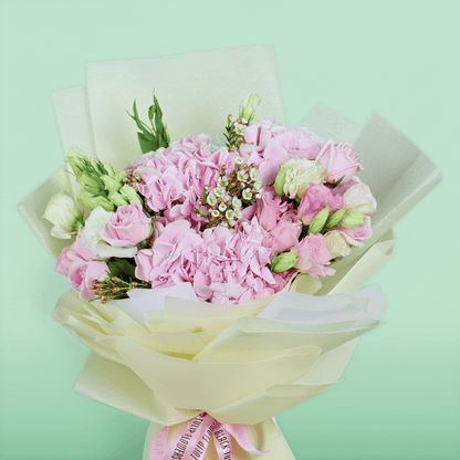 Bouquet of pink hydrangeas, roses, Eustoma and wax flowers arranged in layered ivory non-woven wrapping

