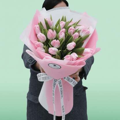 Soft pink tulip bouquet with fresh green foliage in elegant pink and white wrapping.
