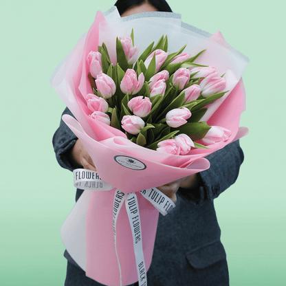 Soft pink tulip bouquet with fresh green foliage in elegant pink and white wrapping.
